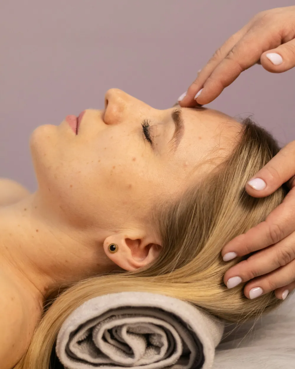 Guest lying face up with her eyes closed while a therapist rests both hands at her hairline during a massage at Yoshino Massage in Arlington, TX